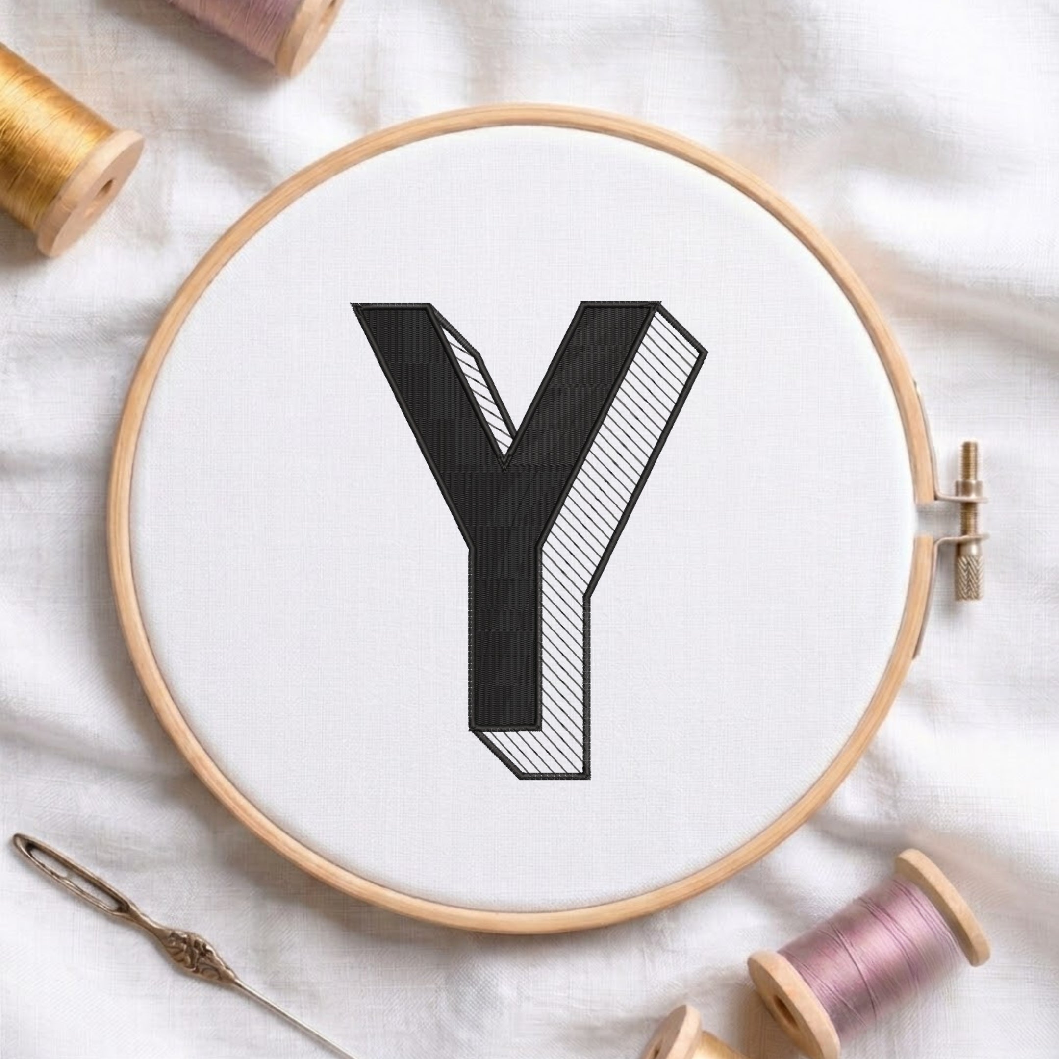 An embroidered 3D block letter "Y" with striped shading texture, stitched inside a wooden hoop on white fabric with sewing threads.