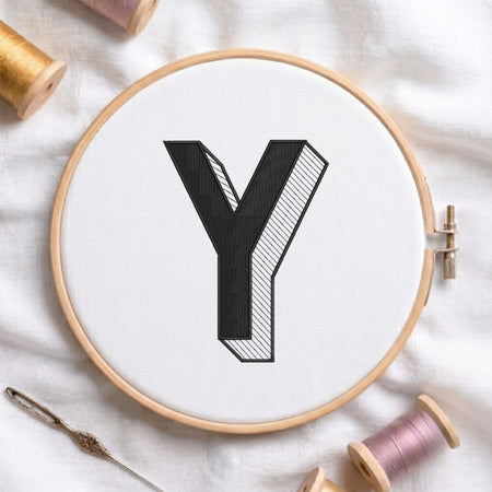 An embroidered 3D block letter "Y" with striped shading texture, stitched inside a wooden hoop on white fabric with sewing threads.