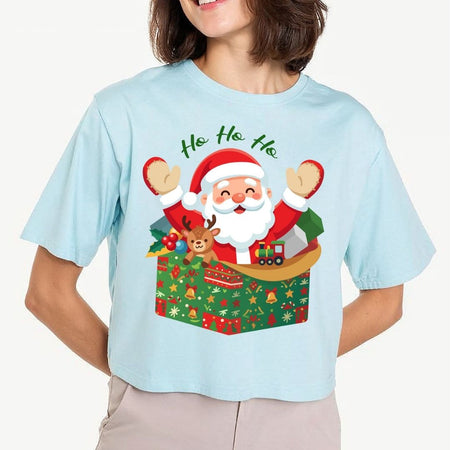 A woman wearing a light blue short-sleeve t-shirt with a colorful graphic of Santa Claus popping out of a gift box with the text 'Ho, Ho, Ho' above him, against a plain light background.