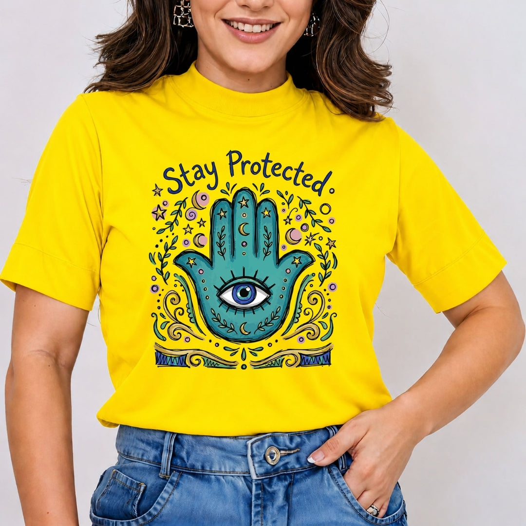 Smiling person wearing a bright yellow t-shirt featuring a detailed teal Hamsa hand with an evil eye and the phrase "Stay Protected".