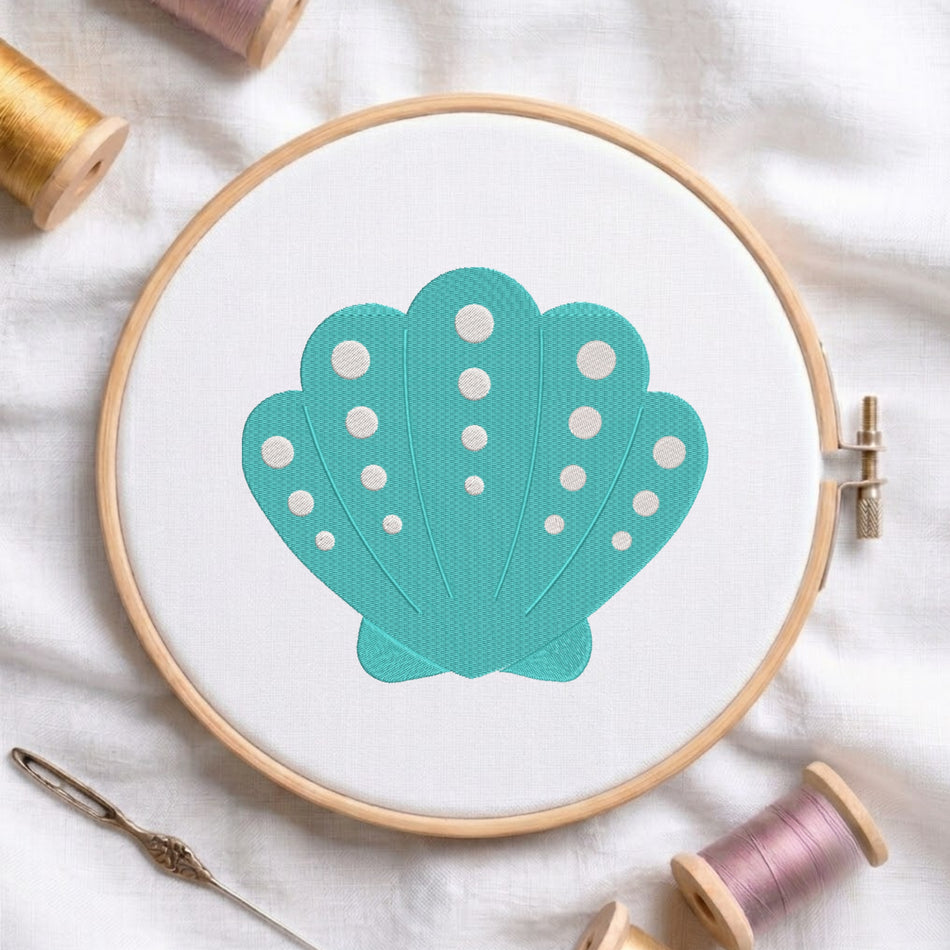 A wooden embroidery hoop holds white fabric with a teal scallop shell design featuring white polka dots. The hoop is styled on a white fabric background with spools of thread and a metal needle.