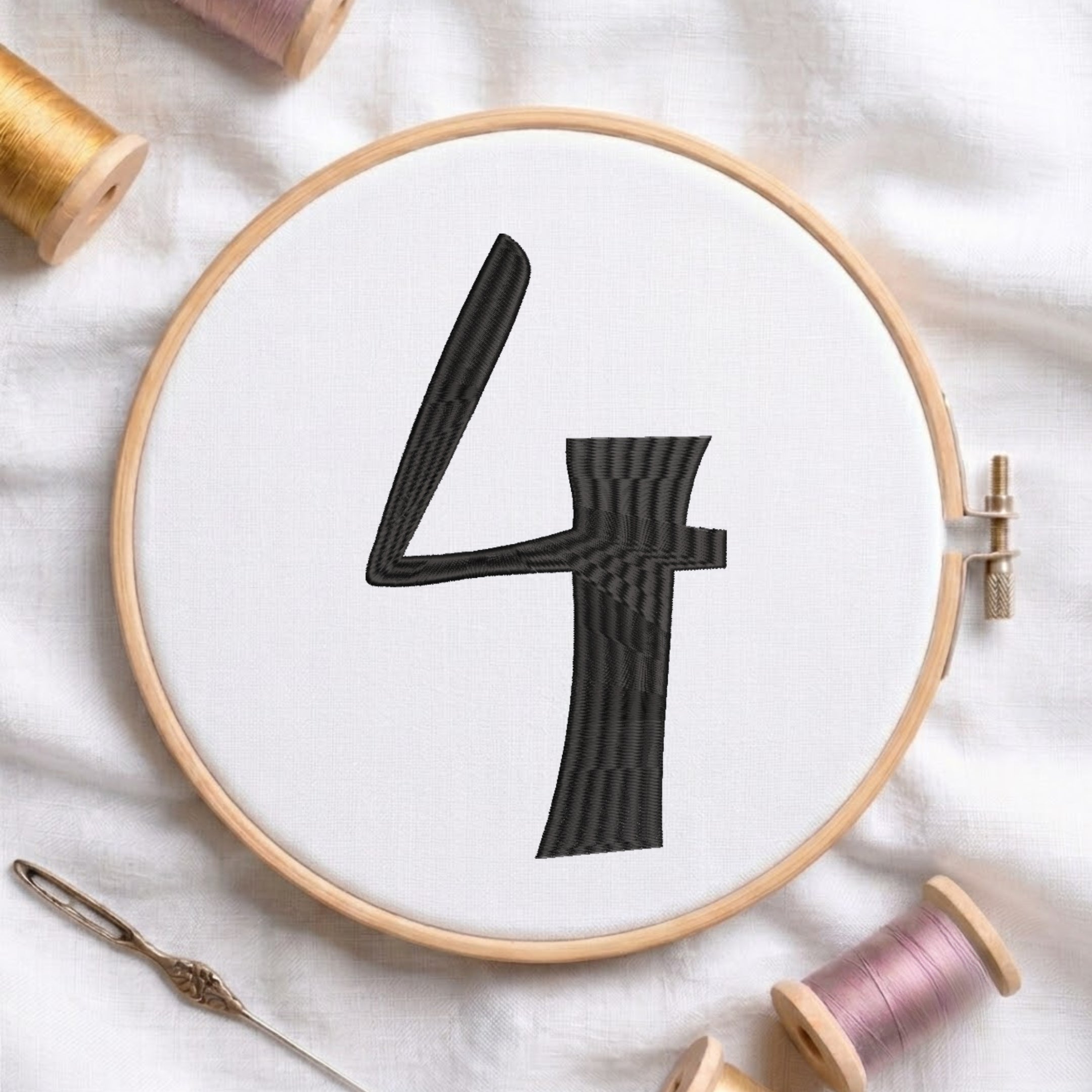 A circular embroidery hoop holding white fabric with a large black stitched number 4, surrounded by spools of thread and a needle on a white fabric background.