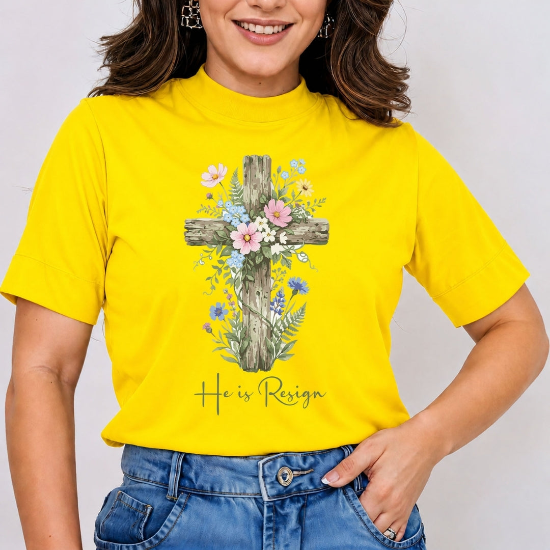 A person wearing a bright yellow t-shirt with a floral cross graphic and the text "He is Resign" printed on the front.