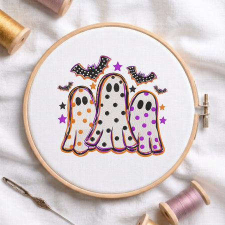 Cute Halloween ghosts and bats machine embroidery design shown in a wooden embroidery hoop on white fabric with thread spools and a needle