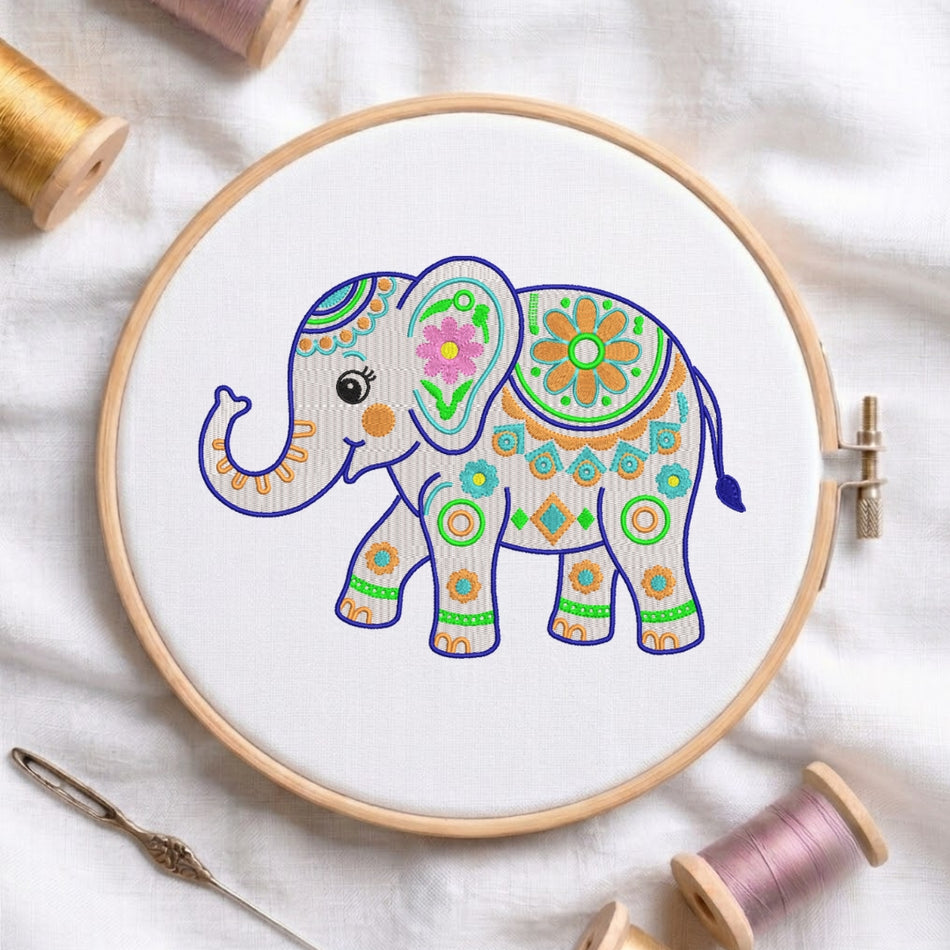 A wooden embroidery hoop holding white fabric with a colorful embroidered elephant design. Spools of thread and a needle are arranged around it on a white fabric background.