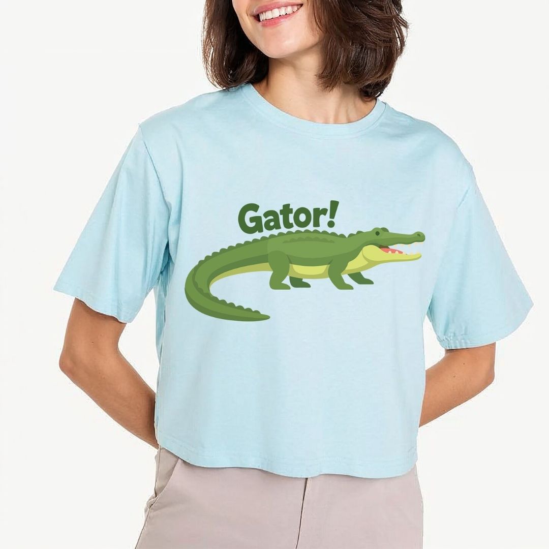 A woman smiling while wearing a light blue cropped t-shirt featuring a cute cartoon green alligator illustration with the text "Gator!" above it.