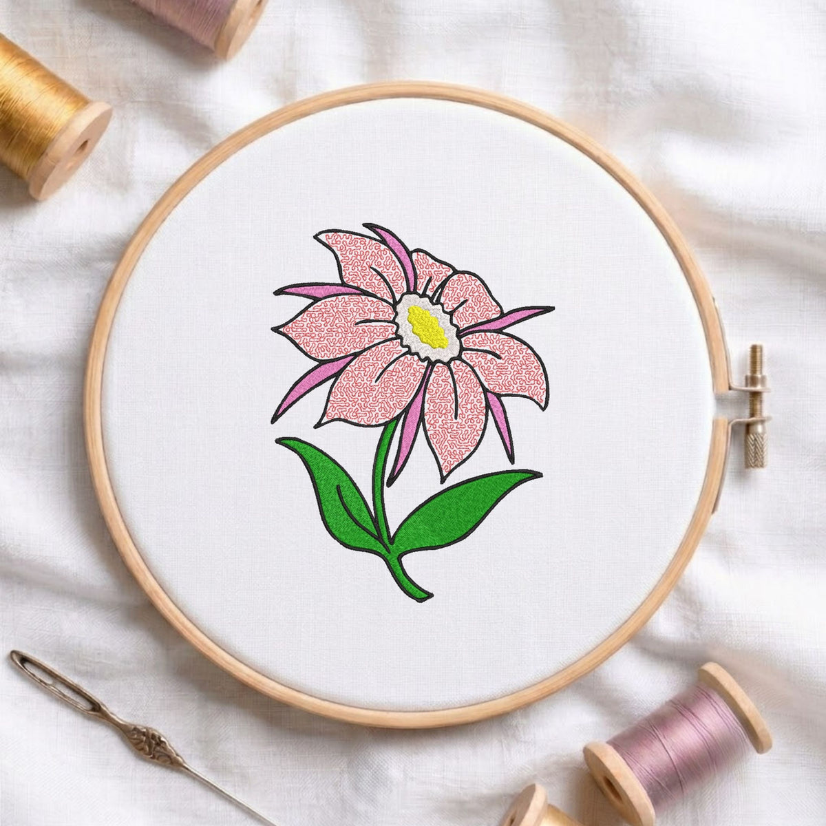 Pink flower machine embroidery design displayed in a wooden hoop on white fabric with thread spools and a needle   