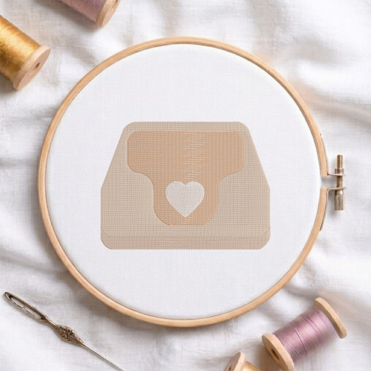 An embroidered heart purse design with a beige handbag and a white heart motif, stitched inside a wooden hoop on white fabric with sewing threads.