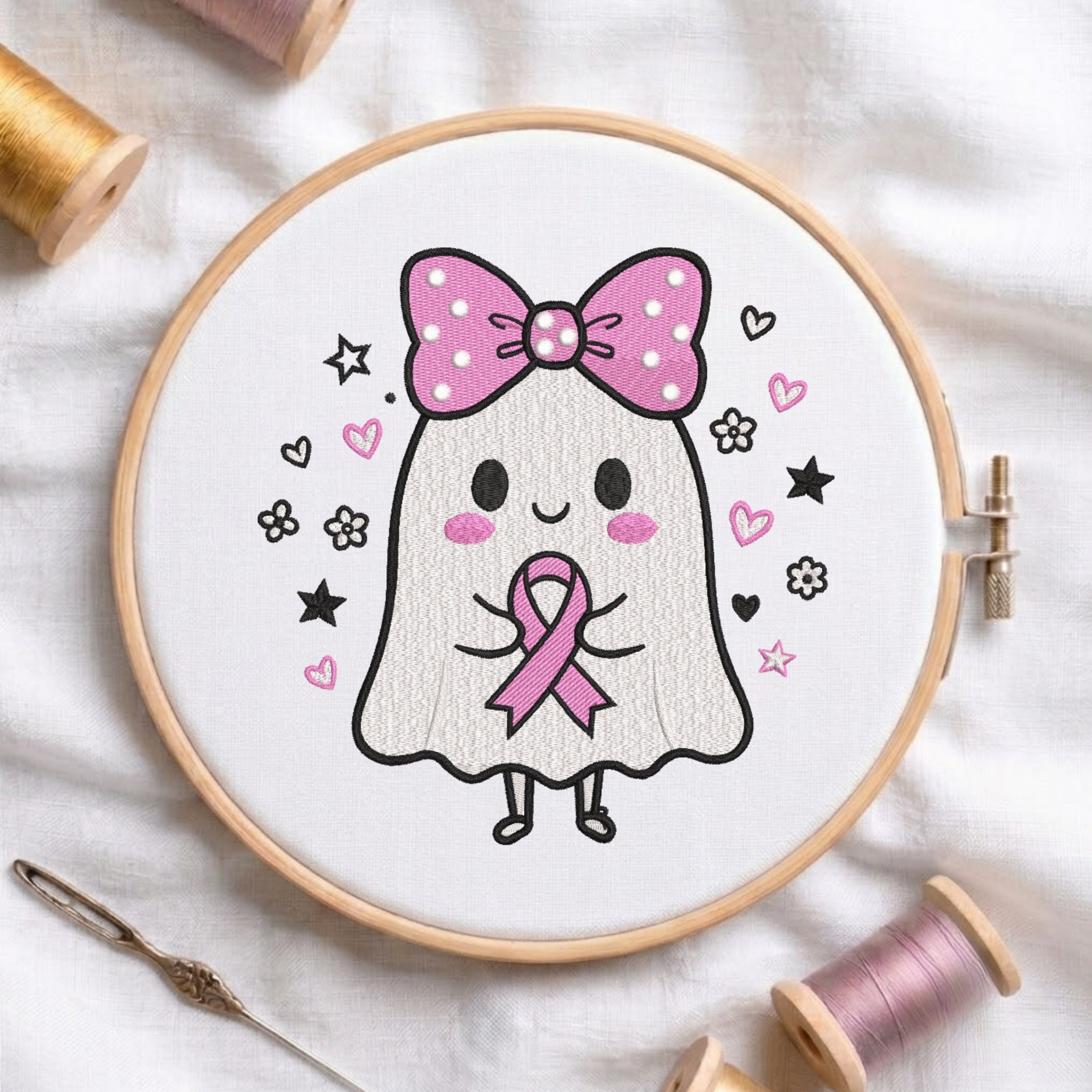 A white fabric stretched in a wooden embroidery hoop, featuring an embroidered cute ghost wearing a polka-dot pink bow, holding a pink awareness ribbon, surrounded by hearts, stars, and flowers.
