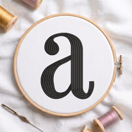 A wooden embroidery hoop holding white fabric with a large black embroidered lowercase letter 'a', styled on a white cloth with spools of thread and a needle around it.