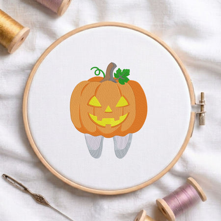 Cute jack-o-lantern pumpkin tooth Halloween dental machine embroidery design shown in a wooden embroidery hoop on white fabric with thread spools and a needle   