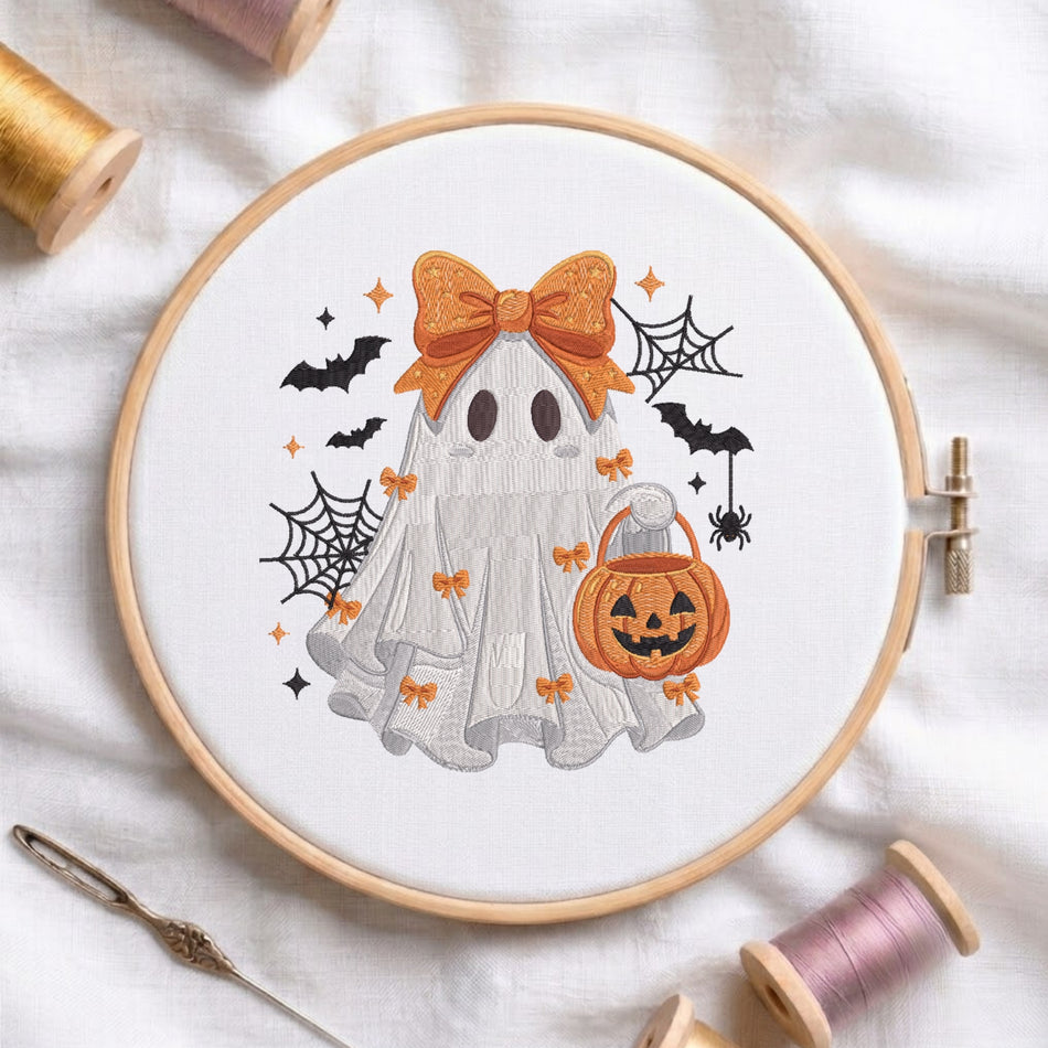 A white fabric stretched in a wooden embroidery hoop, featuring an embroidered cute ghost wearing a large orange bow, holding a jack-o'-lantern pumpkin bucket, surrounded by bats, spiderwebs, and small bows.