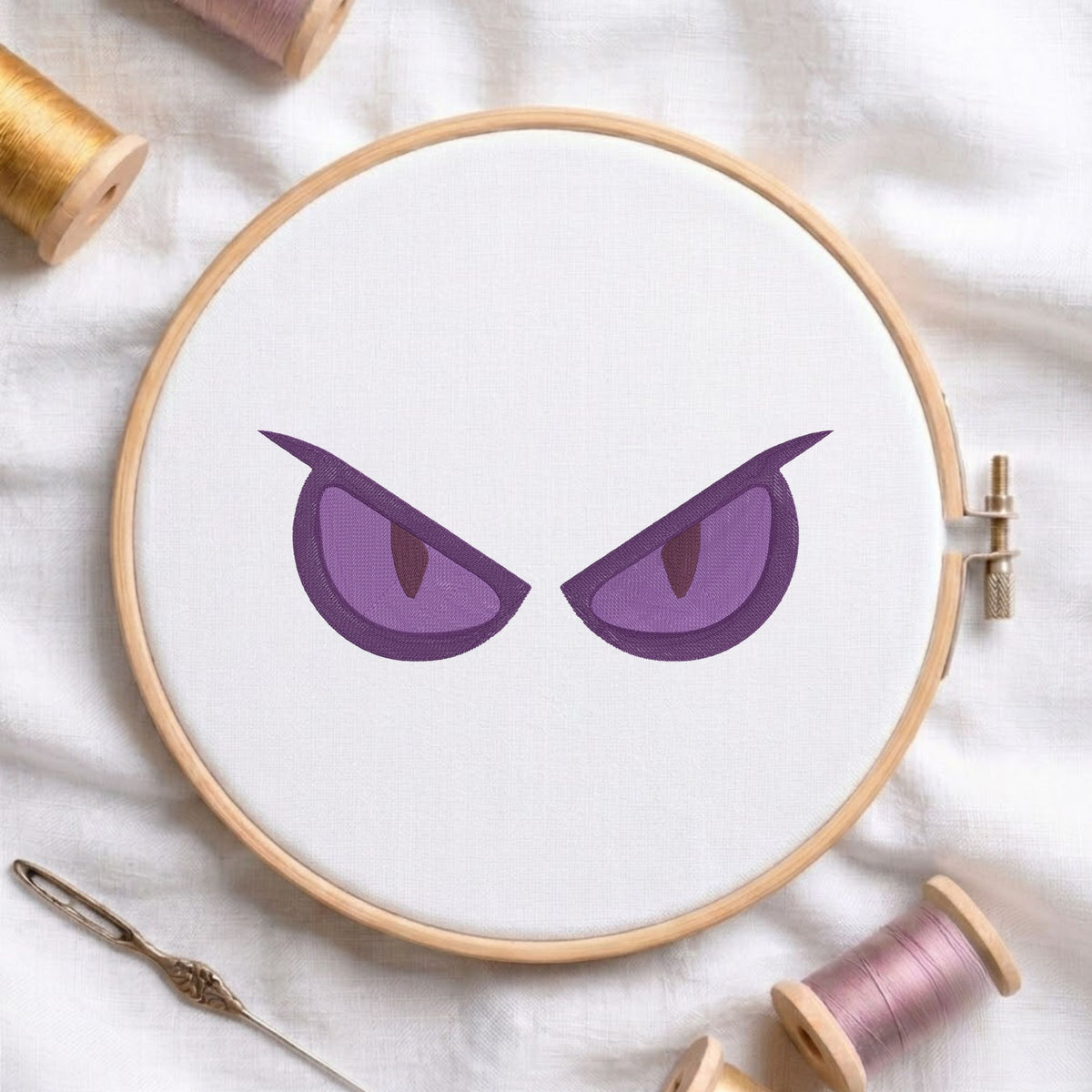 Dark purple expressive evil eyes embroidery pattern displayed inside a wooden embroidery hoop on white fabric.