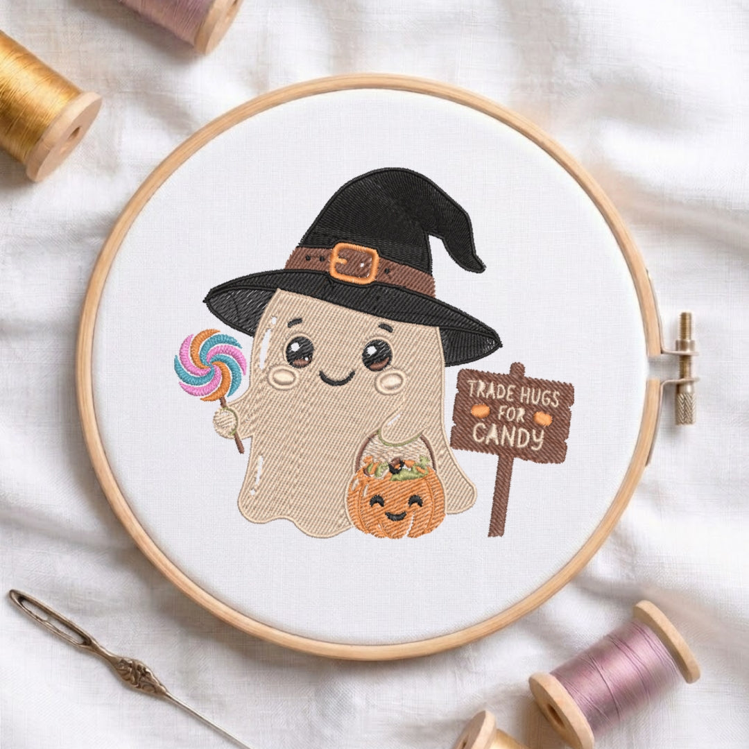 A circular embroidery hoop displays a cute cartoon ghost design with a black witch hat, holding a rainbow lollipop and a small jack-o'-lantern, next to a sign that reads 'TRADE HUGS FOR CANDY'. The hoop is styled on a white fabric background with spools of thread and a needle.