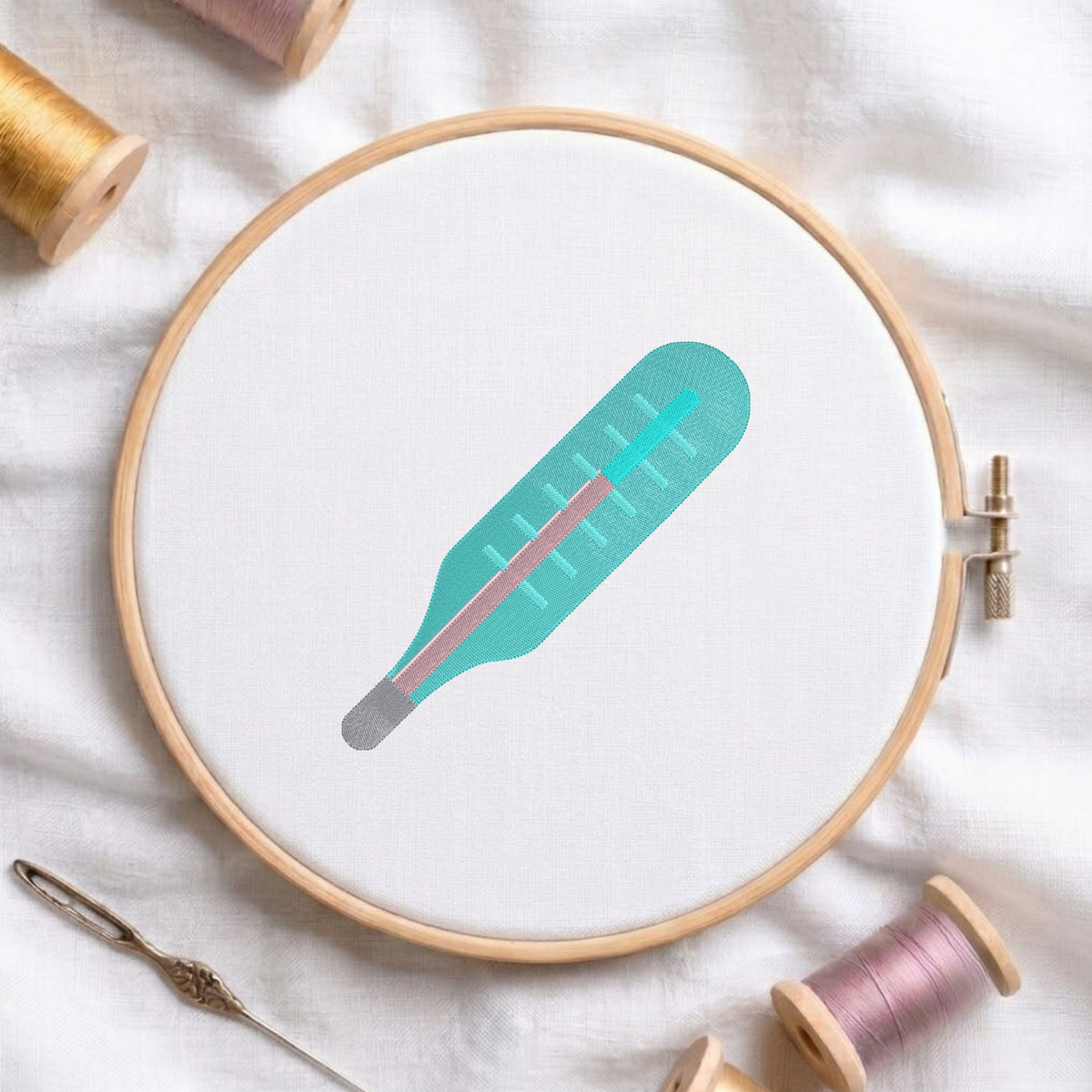 A circular embroidery hoop holding white fabric with a stylized thermometer design in teal, pink, and gray. The hoop is styled on a white fabric background with spools of thread and a needle nearby.