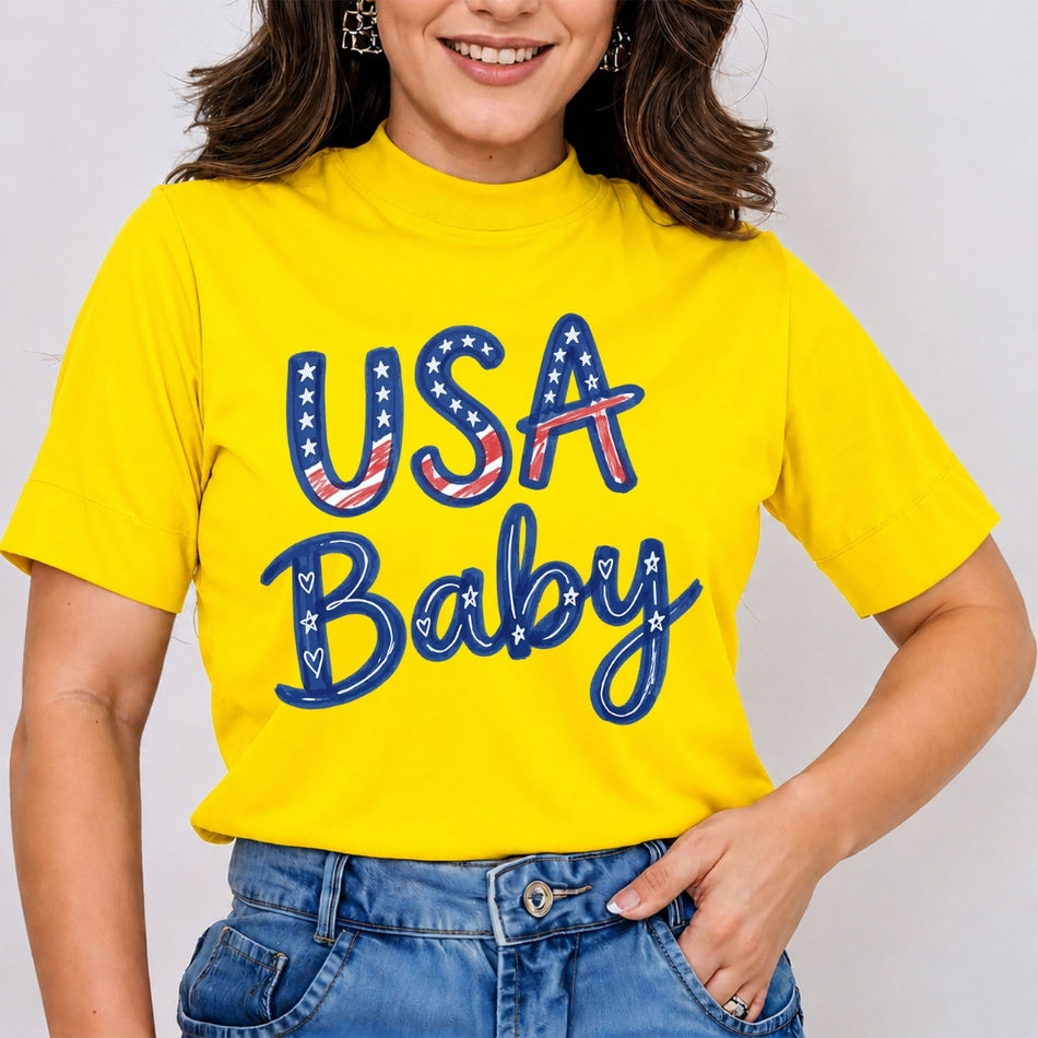 A woman wearing a bright yellow short-sleeve t-shirt with a patriotic graphic that reads 'USA Baby' in blue, red, and white. She is also wearing blue jeans, shown from the chest down against a plain light gray background.