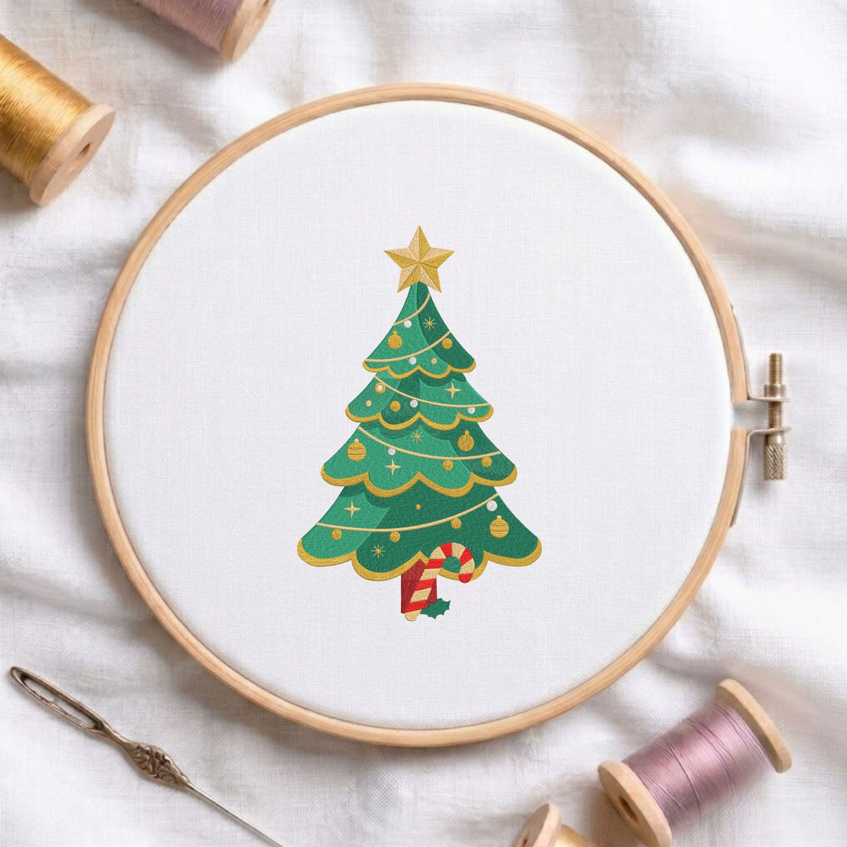 Decorated Christmas tree topped with a golden star and candy cane trunk machine embroidery design shown in a wooden embroidery hoop on white fabric with thread spools and a needle   