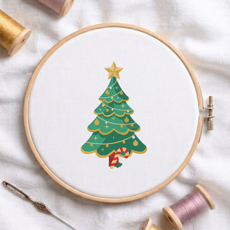 Decorated Christmas tree topped with a golden star and candy cane trunk machine embroidery design shown in a wooden embroidery hoop on white fabric with thread spools and a needle   