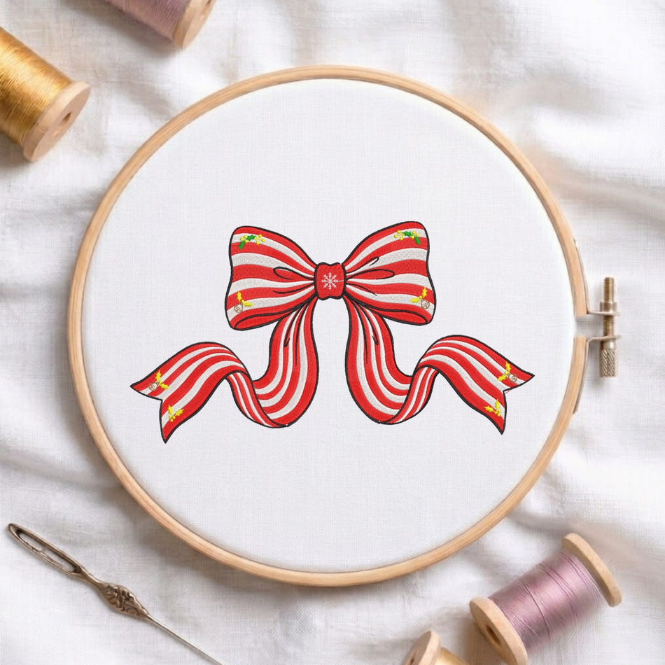 A red and white striped holiday ribbon bow embroidery design displayed in a wooden hoop, accompanied by sewing tools and thread.