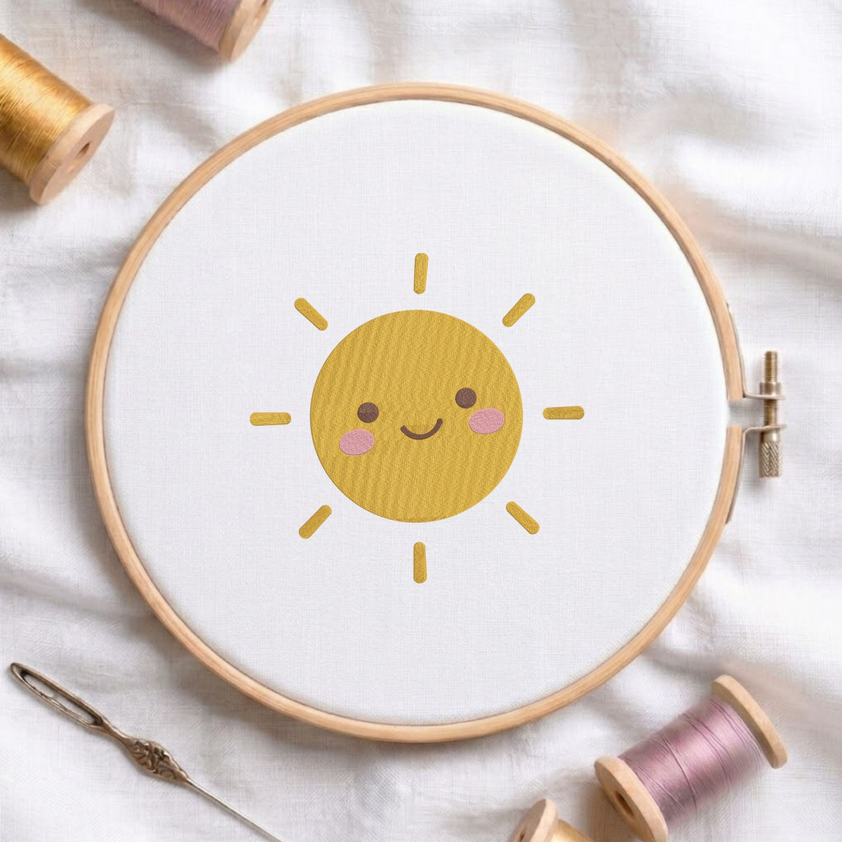 Cute smiling sun machine embroidery design shown in a wooden embroidery hoop on white fabric with thread spools and a needle   