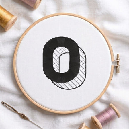 A wooden embroidery hoop holding white fabric with a black outlined letter 'O' design, surrounded by spools of thread and a needle on a white fabric background.
