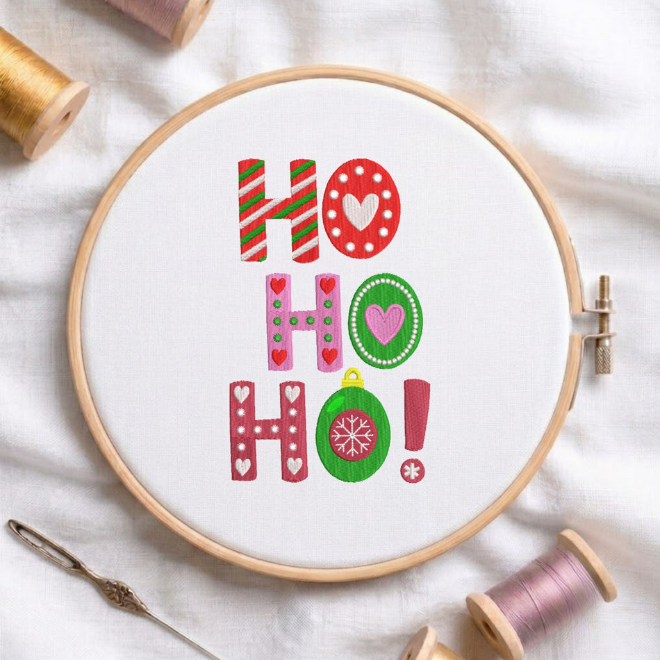A white fabric stretched in a wooden embroidery hoop, featuring embroidered Christmas "HO HO HO!" lettering styled with candy cane stripes, festive hearts, and a green ornament bauble with a snowflake.