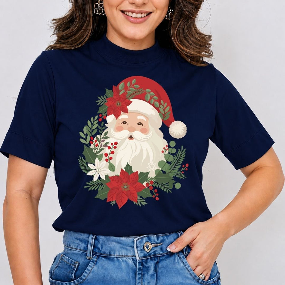 A woman wearing a navy blue short-sleeve t-shirt with a festive Christmas graphic of Santa Claus surrounded by a wreath of red poinsettias, green pine branches, and white flowers. She is also wearing blue jeans against a plain light gray background.