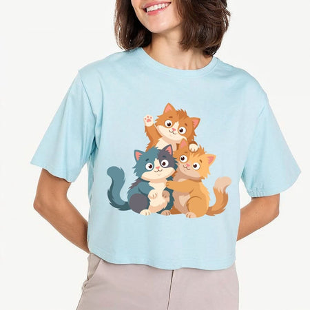 Woman wearing a light blue cropped t-shirt featuring a cute cartoon cats trio sublimation graphic with a waving kitten and hugging cats.