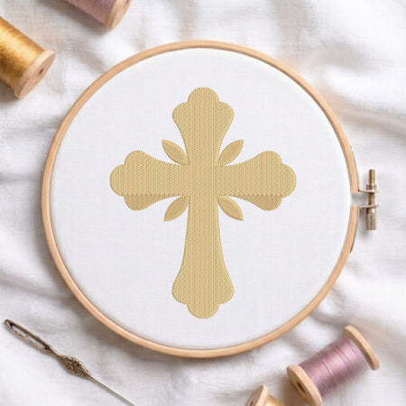 Soft gold ornamental cross pattern with leaf rays embroidered on white fabric in a round wooden embroidery hoop.