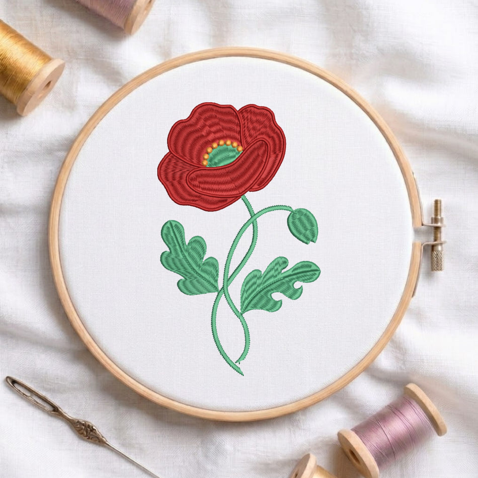 A wooden embroidery hoop holding white fabric with a stitched poppy design in red, green, and yellow, surrounded by spools of thread and a needle on a white fabric background.