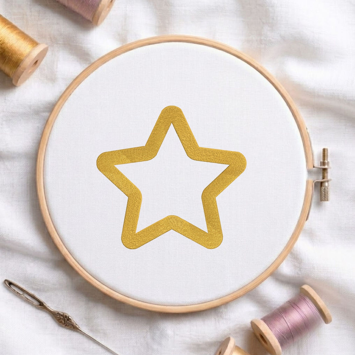Golden star outline machine embroidery design displayed in a wooden hoop on white fabric with thread spools and a needle   