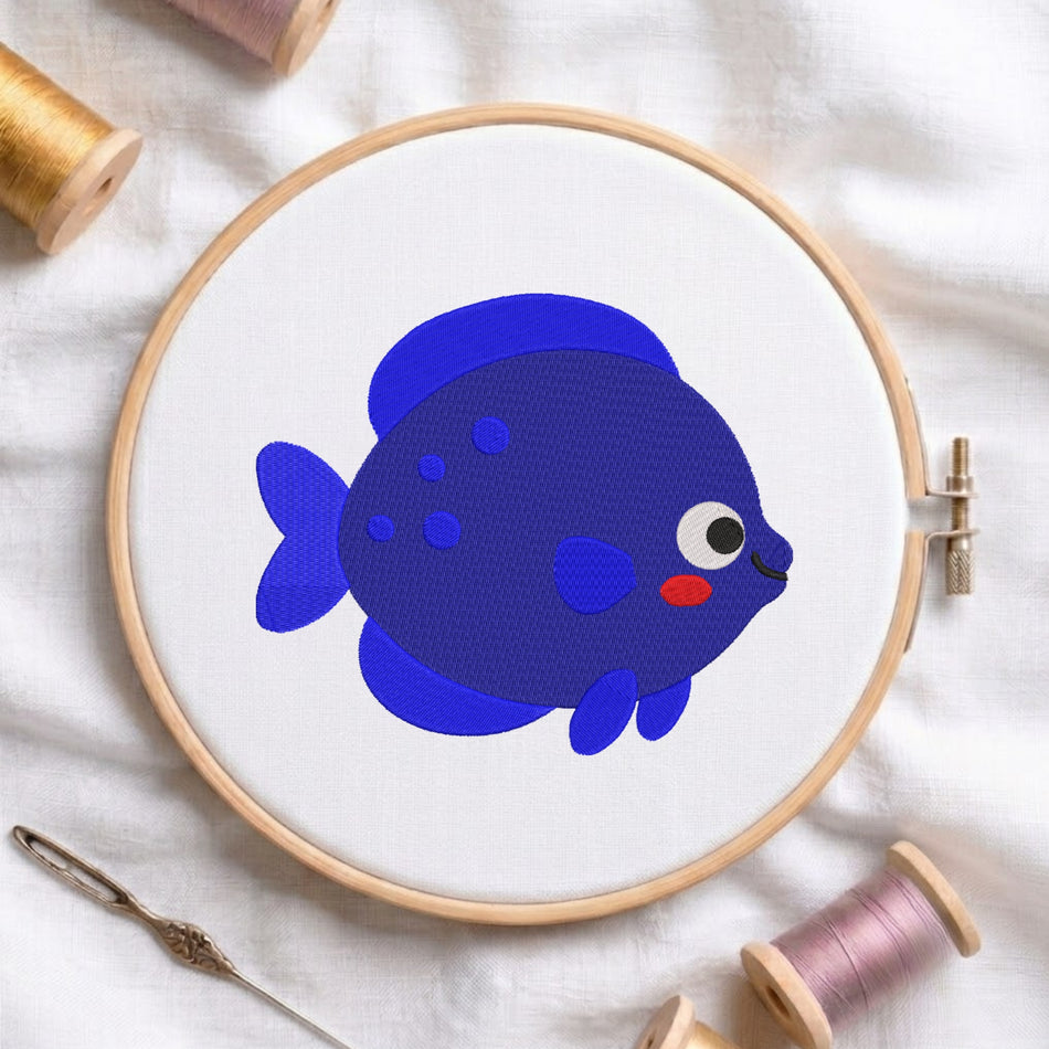 A wooden embroidery hoop holding white fabric with a blue cartoon fish design, surrounded by spools of thread and a needle on a white cloth background.