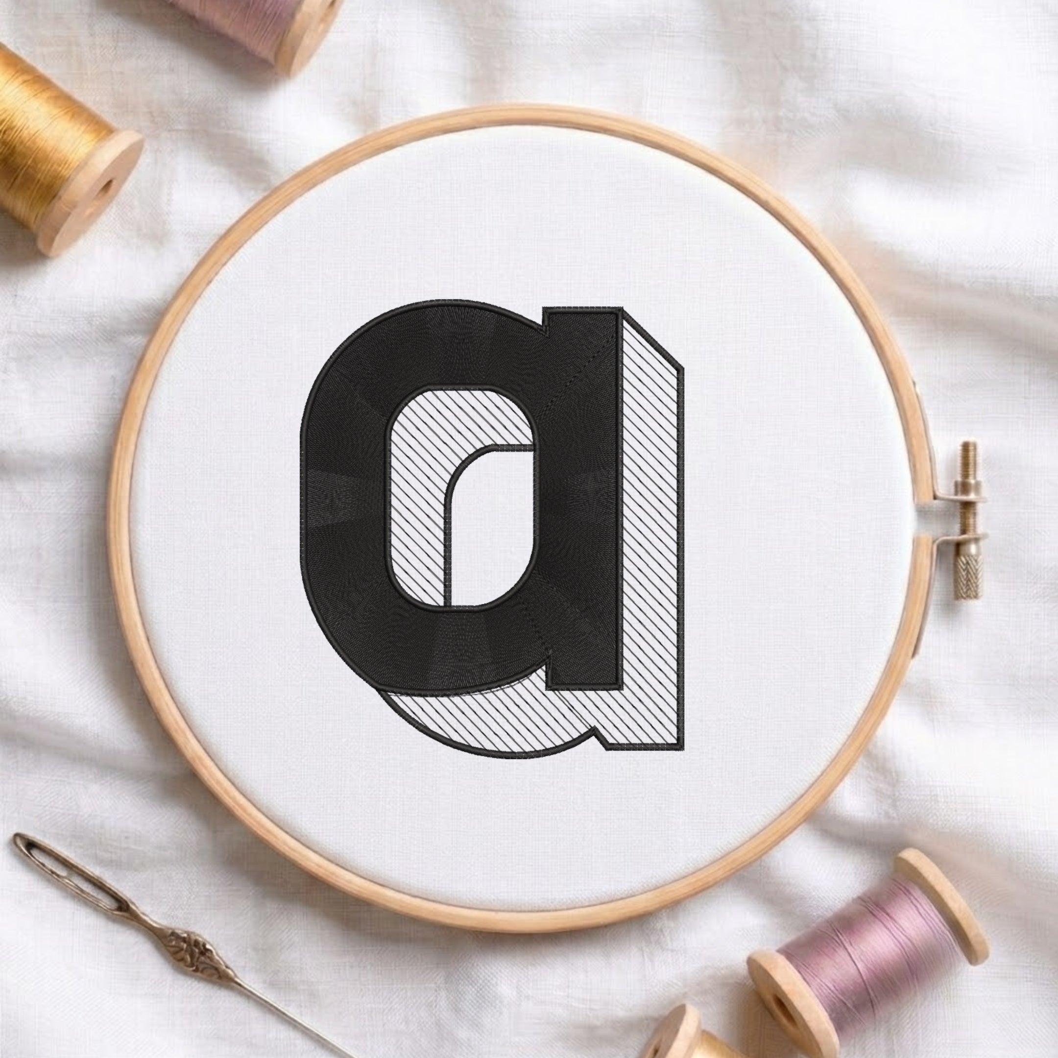 An embroidered 3D block lowercase letter "a" with striped shading texture, stitched inside a wooden hoop on white fabric with sewing threads.