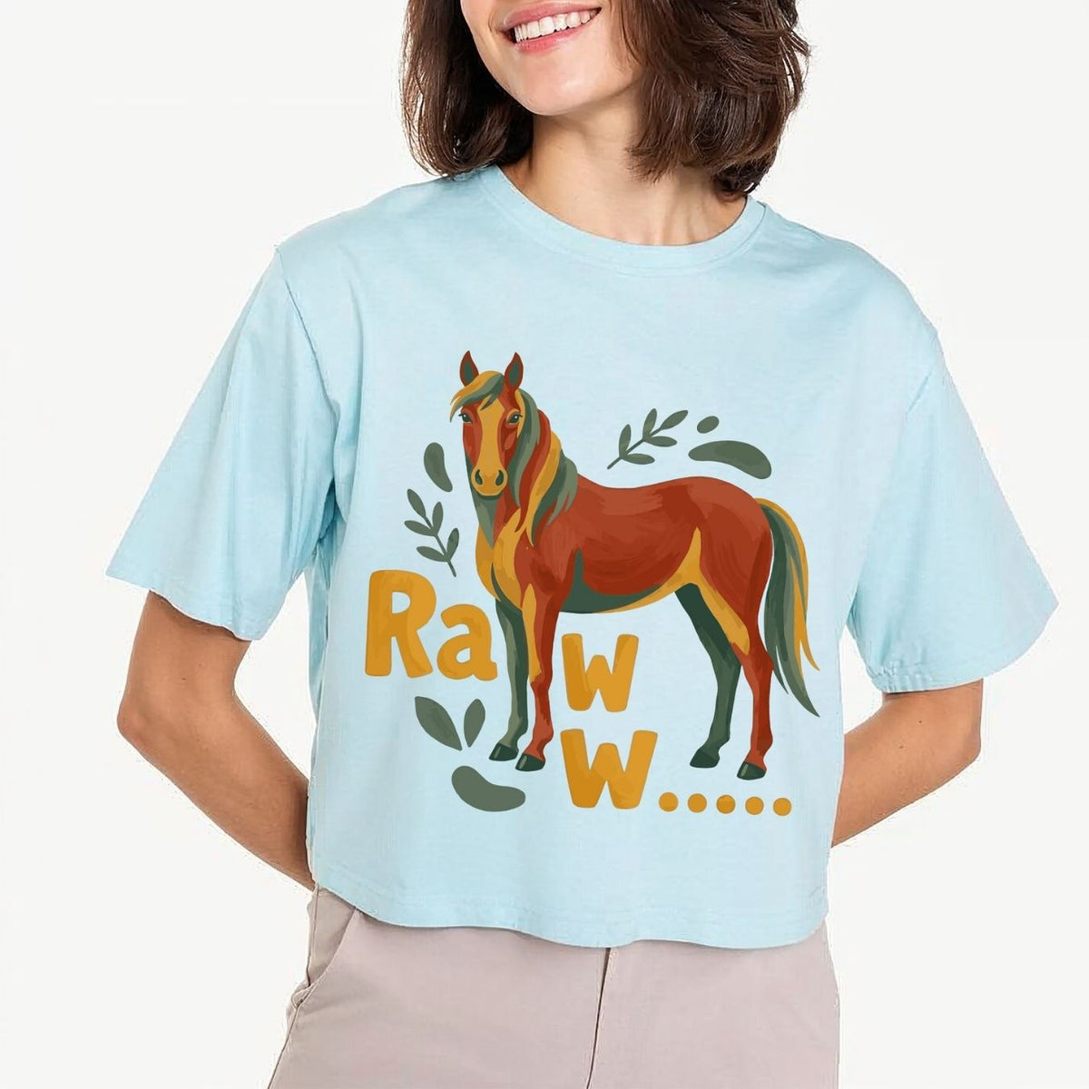 A woman modeling a light pastel blue crop top t-shirt featuring a large brown and green watercolor horse illustration with the text "Raww...".