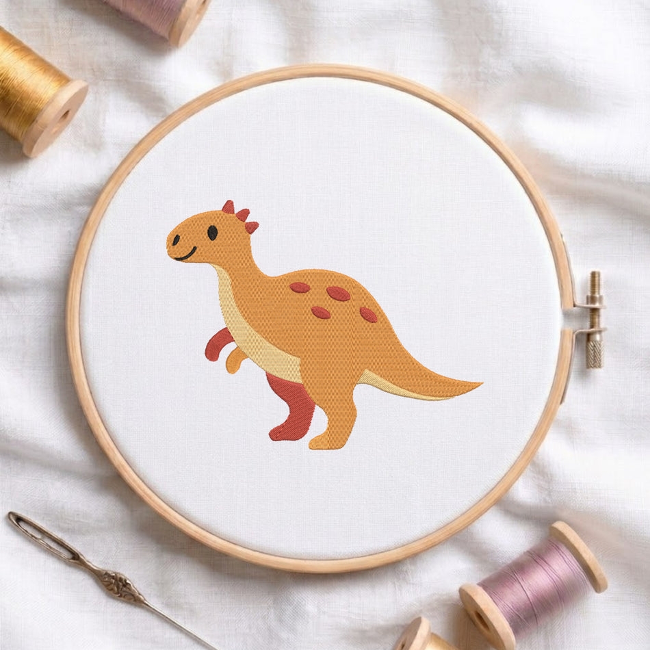 An embroidery hoop on a white cloth displays a finished embroidery design of a cute orange dinosaur with red spots and spikes, flanked by spools of thread and a needle.
