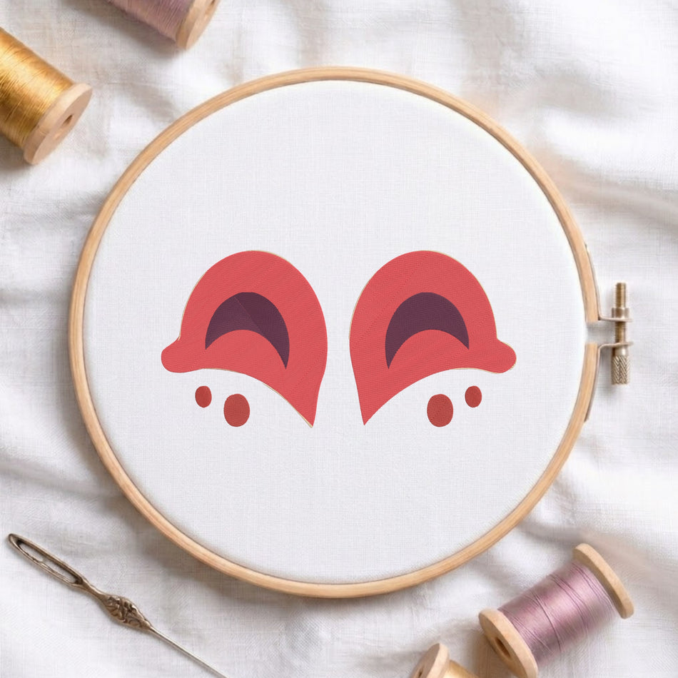 Pinkish coral and dark purple animal ears embroidery pattern centered in a round wooden hoop with thread spools.