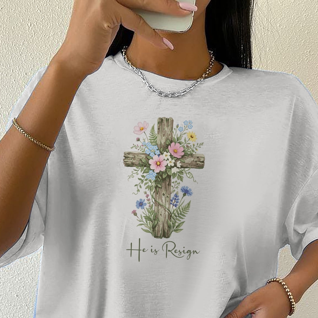 Person wearing a white t-shirt with a floral cross design and 'He is Resign' text.