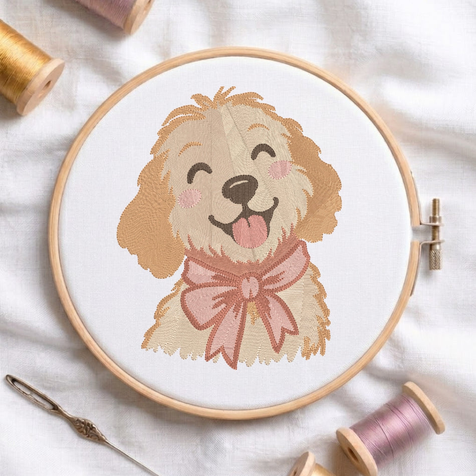 A circular embroidery hoop holding a white fabric with a stitched illustration of a smiling tan dog wearing a pink bow. The hoop is photographed on a white fabric background with spools of thread and a needle around it.