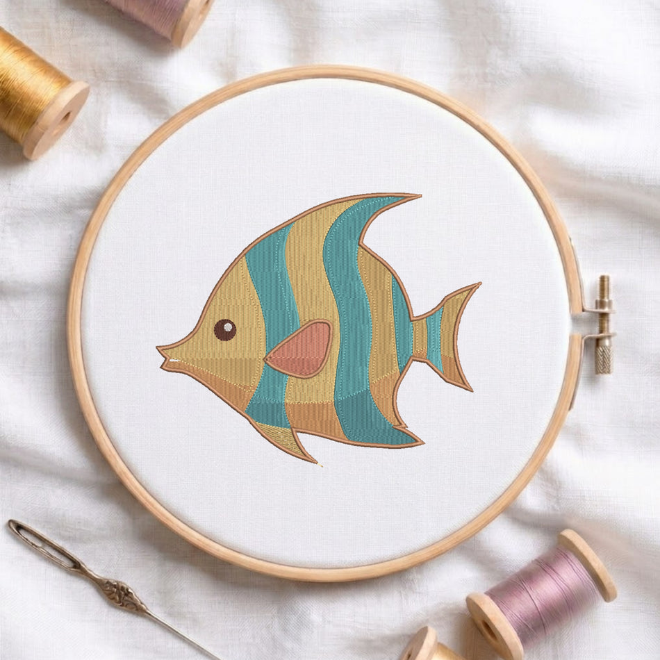 A wooden embroidery hoop holds white fabric with a stylized embroidered fish design in teal, mustard, peach, and brown. The hoop is styled on a white fabric background with spools of thread and a needle.
