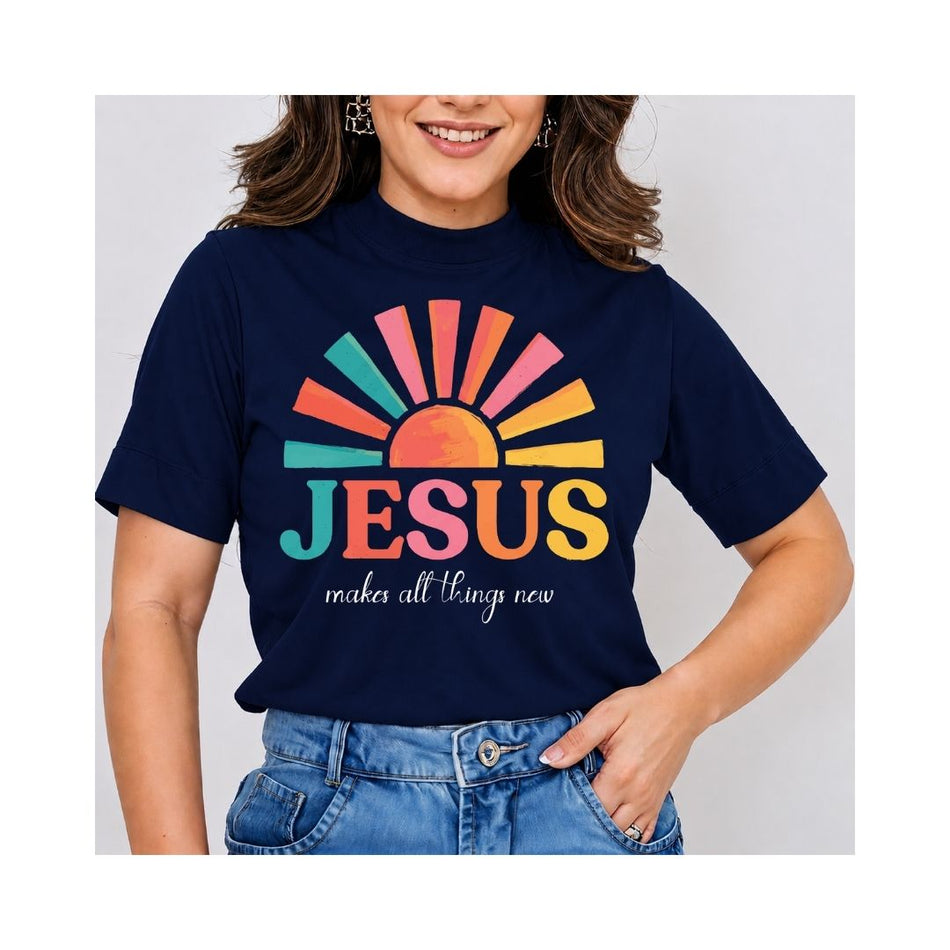A woman wearing a navy blue graphic t-shirt with a colorful sunburst and the text 'JESUS makes all things new' in pink, orange, yellow, and teal, paired with blue jeans.