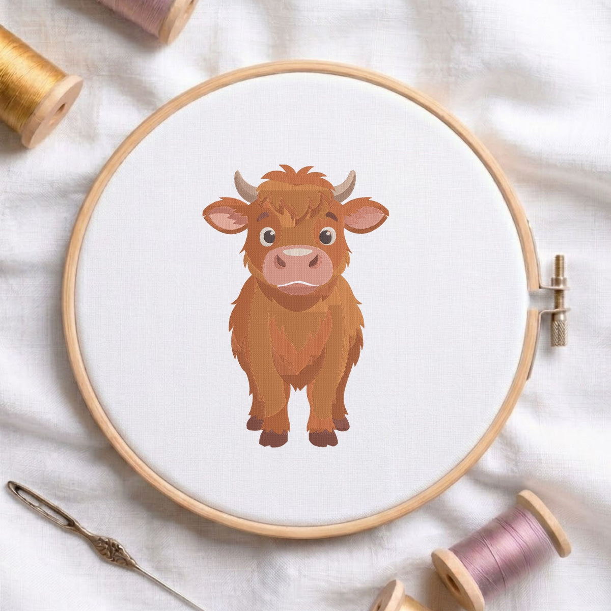 Cute Highland cow machine embroidery design shown in a wooden embroidery hoop on white fabric with thread spools and a needle