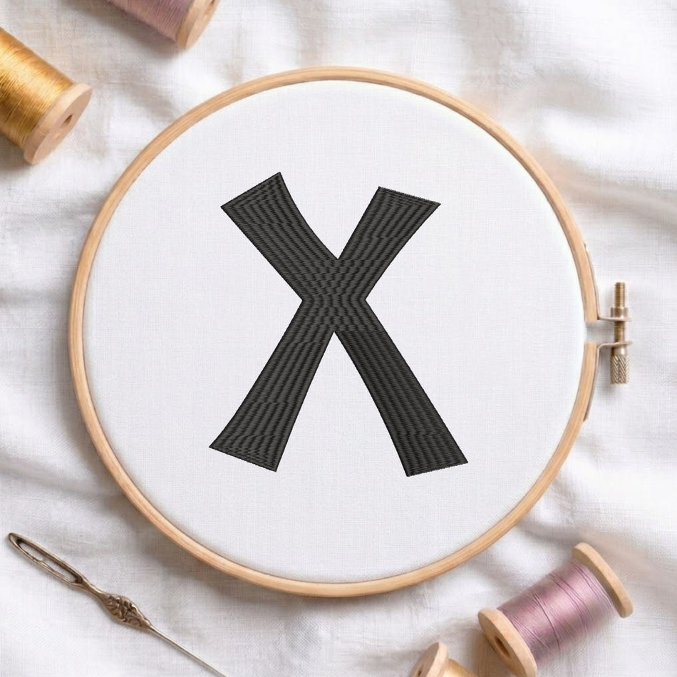 A wooden embroidery hoop holding white fabric with a large black embroidered letter X, styled on a white cloth with spools of thread and a needle.