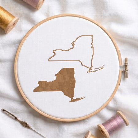 New York state map fill and outline machine embroidery design, displayed in a wooden hoop on white fabric with thread spools and a needle.