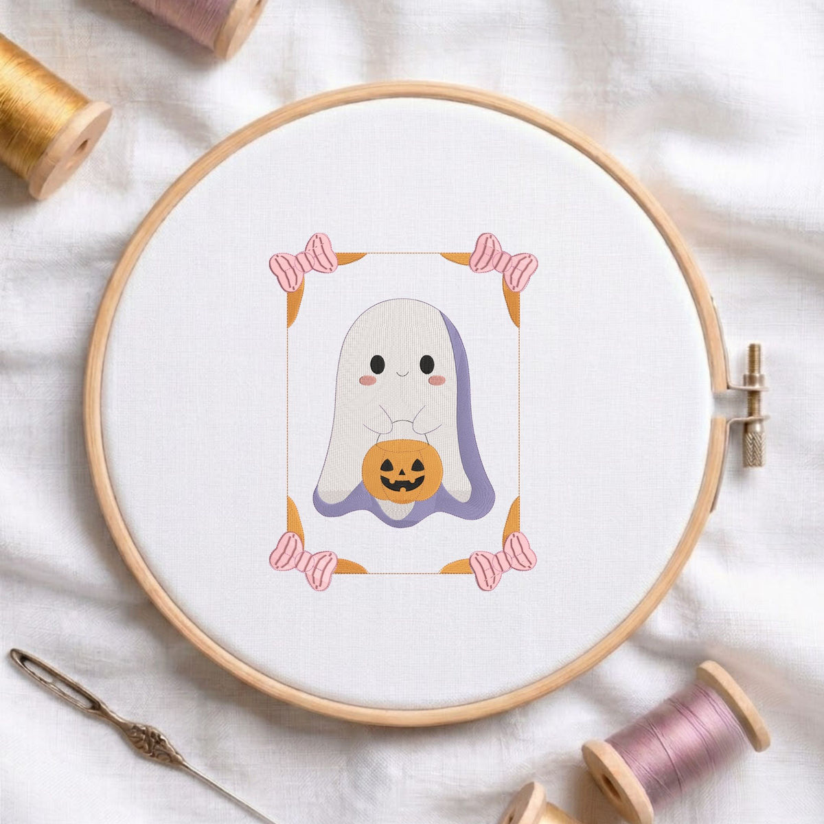 Cute ghost holding a jack-o-lantern pumpkin machine embroidery design displayed in a wooden embroidery hoop on white fabric with thread spools and a needle