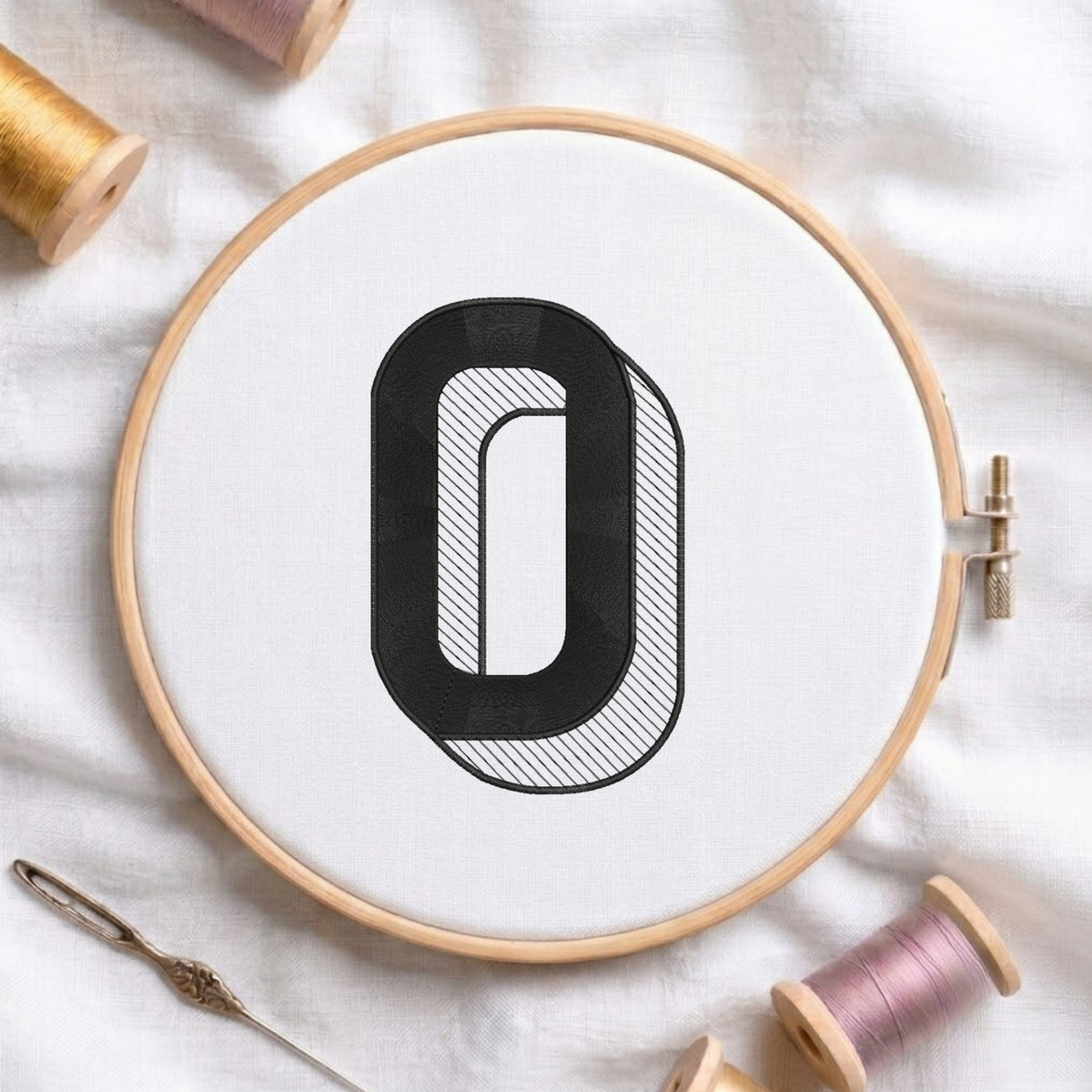 An embroidered 3D block letter "O" with striped shading texture, stitched inside a wooden hoop on white fabric with sewing threads.