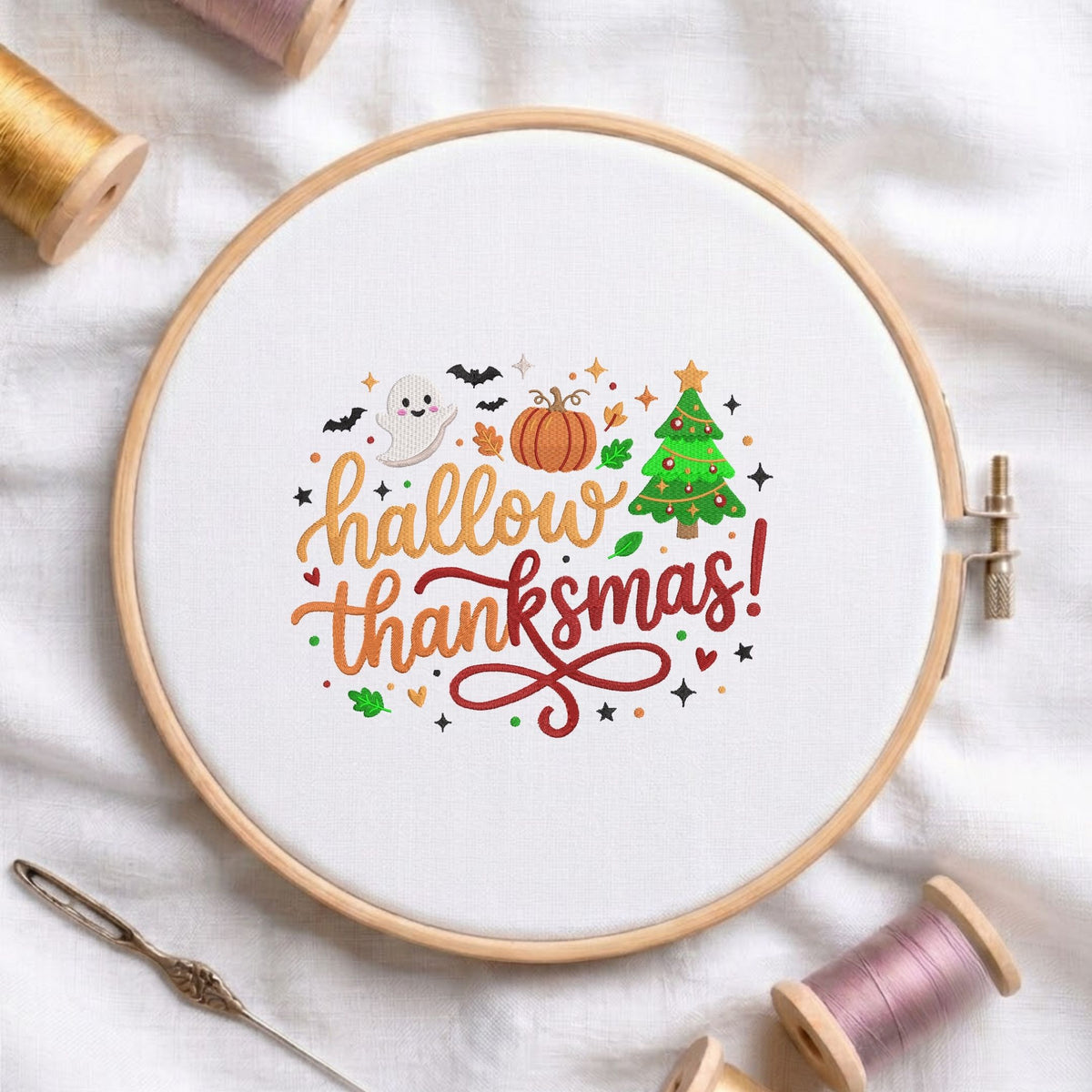 "Hallowthanksmas!" holiday mashup machine embroidery design with a ghost, pumpkin, and Christmas tree displayed in a wooden hoop on white fabric with thread spools and a needle