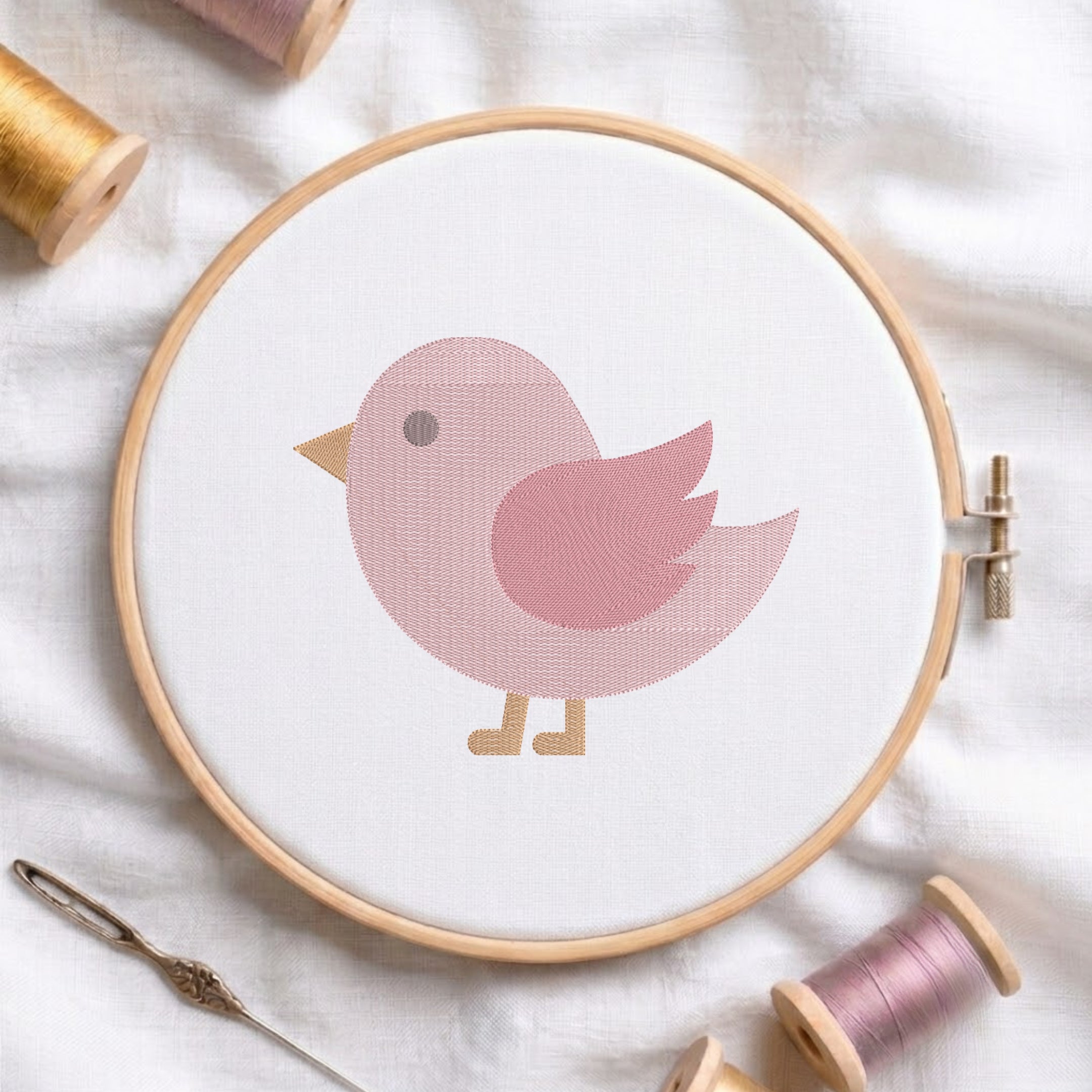 An embroidered pink bird design with yellow beak and feet, stitched inside a wooden hoop on white fabric with sewing threads.
