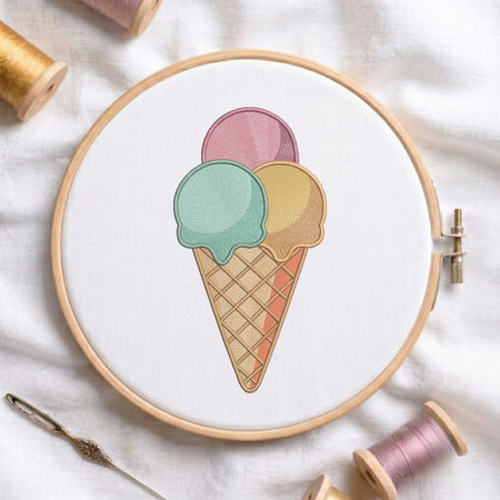A circular embroidery hoop holding white fabric with a pastel ice cream cone design, surrounded by spools of thread and a needle on a white fabric background.
