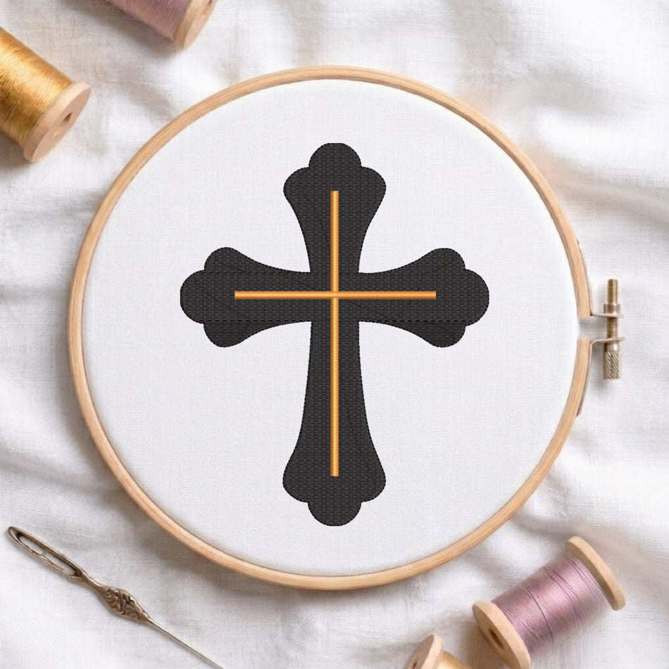 An embroidery hoop on a white cloth displays a finished embroidery design of an ornate black cross with gold intersecting lines, flanked by spools of thread and a needle.