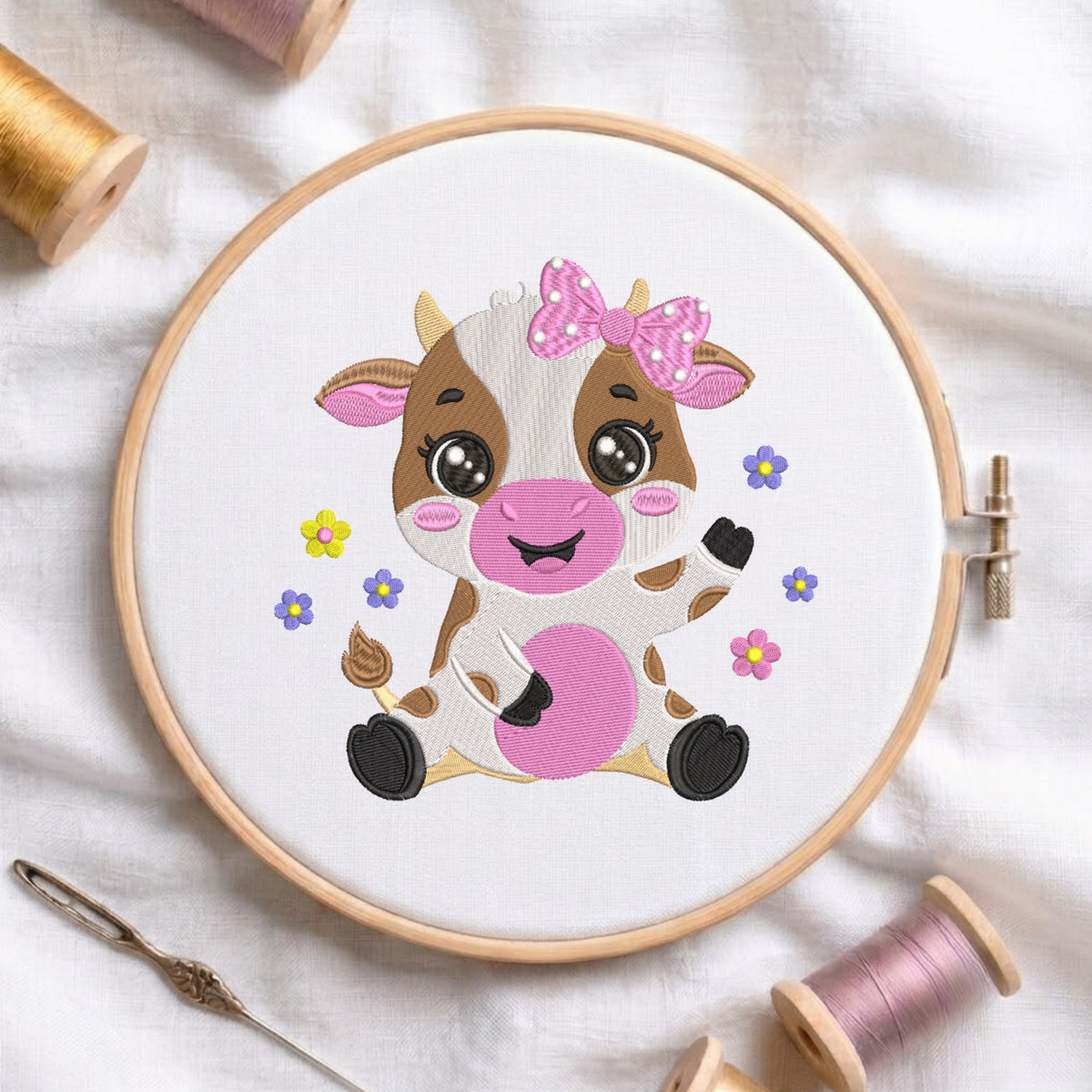 An embroidered design of a cute sitting baby cow with brown patches, big shiny eyes, a pink floral bow, and colorful flowers, stitched inside a wooden hoop on white fabric with sewing threads.
